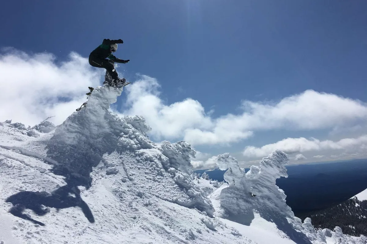 A dynamic shot of a snowboarder mid-jump against a snowy mountain peak and dramatic clouds. The winter landscape conveys a sense of adventure and the possibilities for active outdoor pursuits just a short drive away.