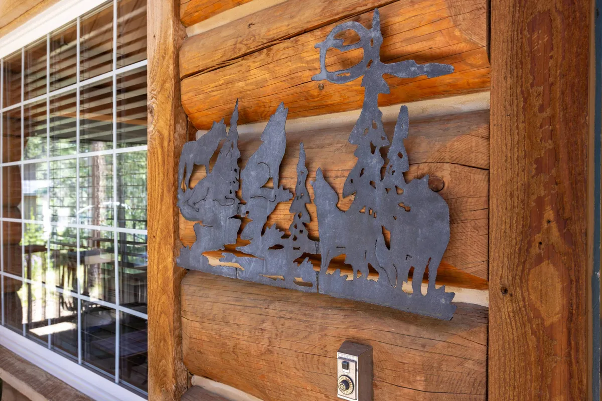 A cozy nook with a large window framed by log walls, metal art silhouette, and soft light pouring in. The space blends craftsmanship with comfort, offering a tranquil setting for work or relaxation while admiring the view outside.