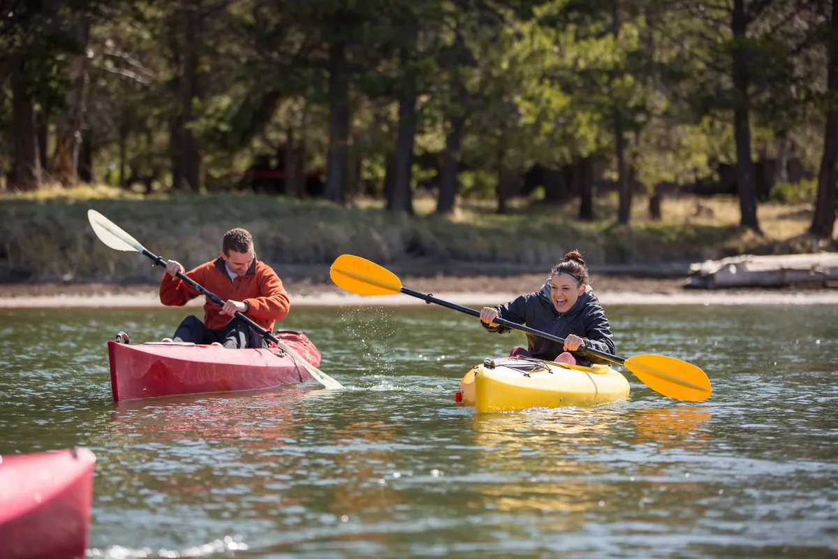 This exterior image features two kayakers gliding across a calm body of water, surrounded by reflections and natural scenery. The brightly colored kayaks and the joyful expressions of the participants evoke a sense of adventure and fun in the outdoors.