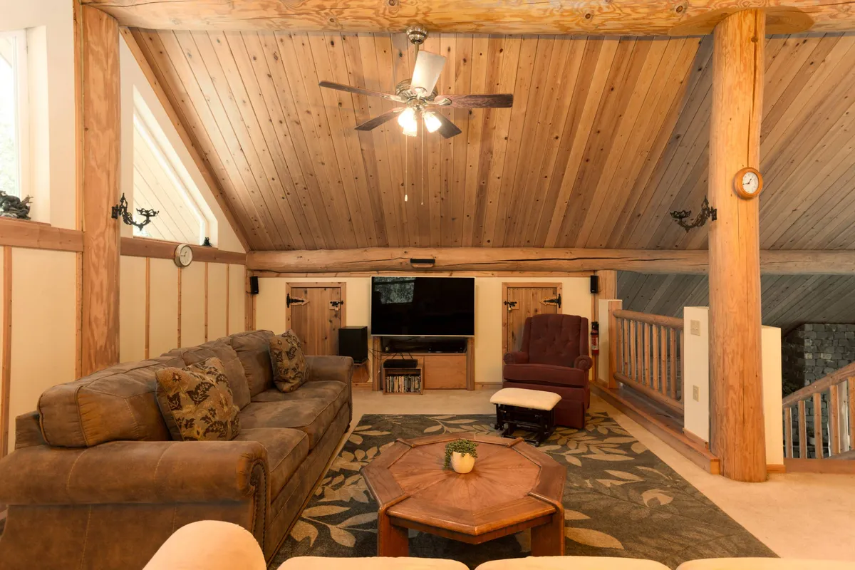 A welcoming living room space with a comfortable sofa, armchair, area rug, television, and striking wooden ceiling beams. The layout invites guests to relax, watch TV, or socialize in a cozy, well-lit environment.